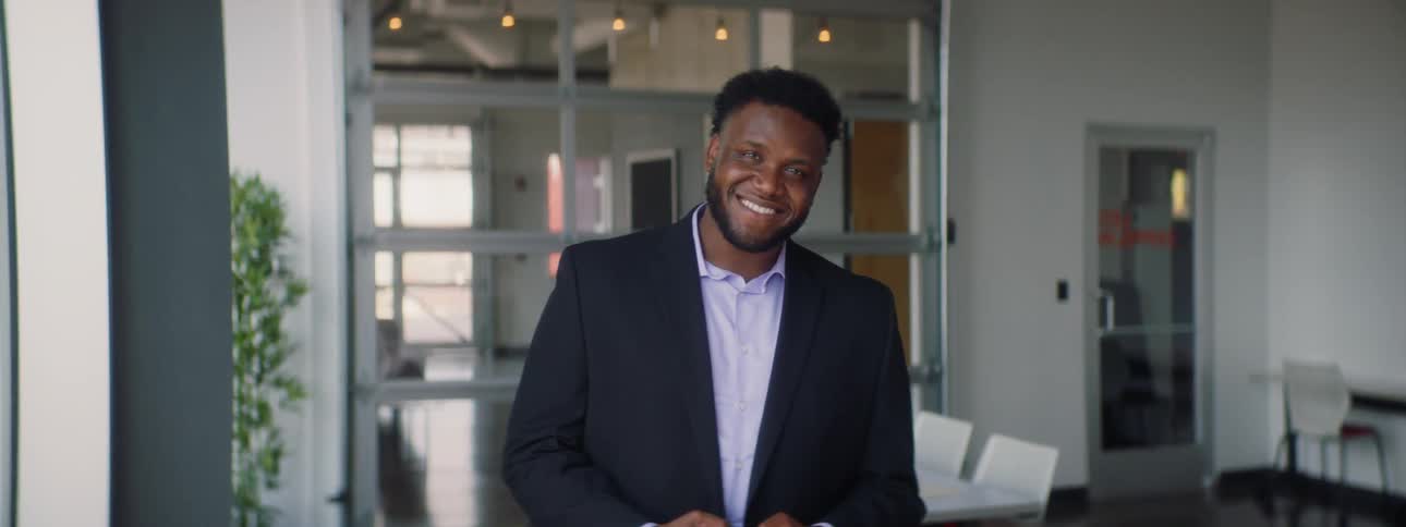 A man in a suit looks up while using a phone and smiles