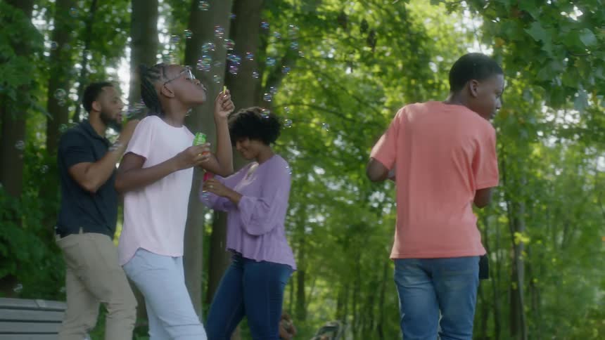 Family is blowing bubbles at each other in shady park