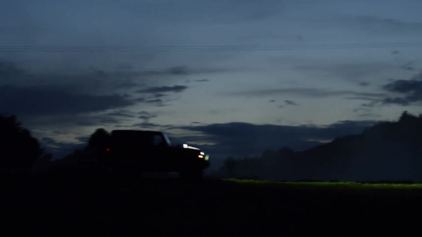 A jeep drives across grass at night
