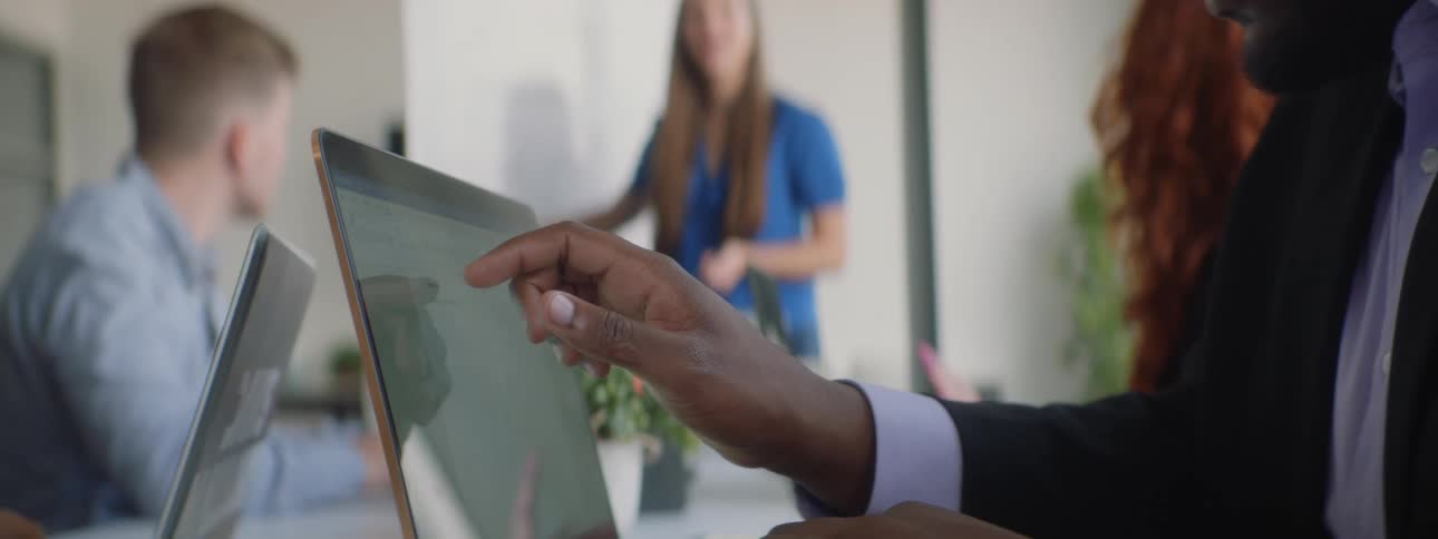 A man is using a laptop in a room filled with people