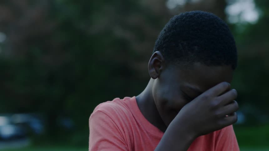 A young man is laughing and covering his face near a wooded area
