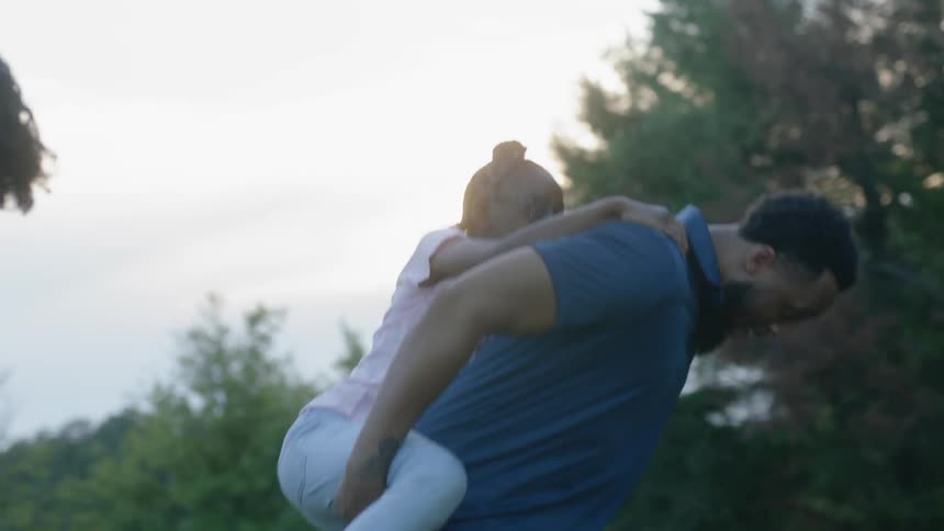 A family of 3 walking through a park with the little girl riding on dad's back