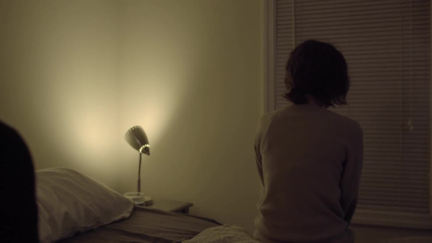 Woman is sitting on bed facing the wall