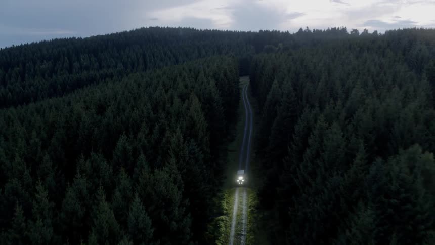 An aerial view of a vehicle going through a forest road