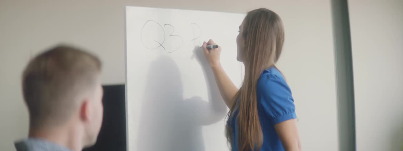 A woman writes on a whiteboard in a meeting