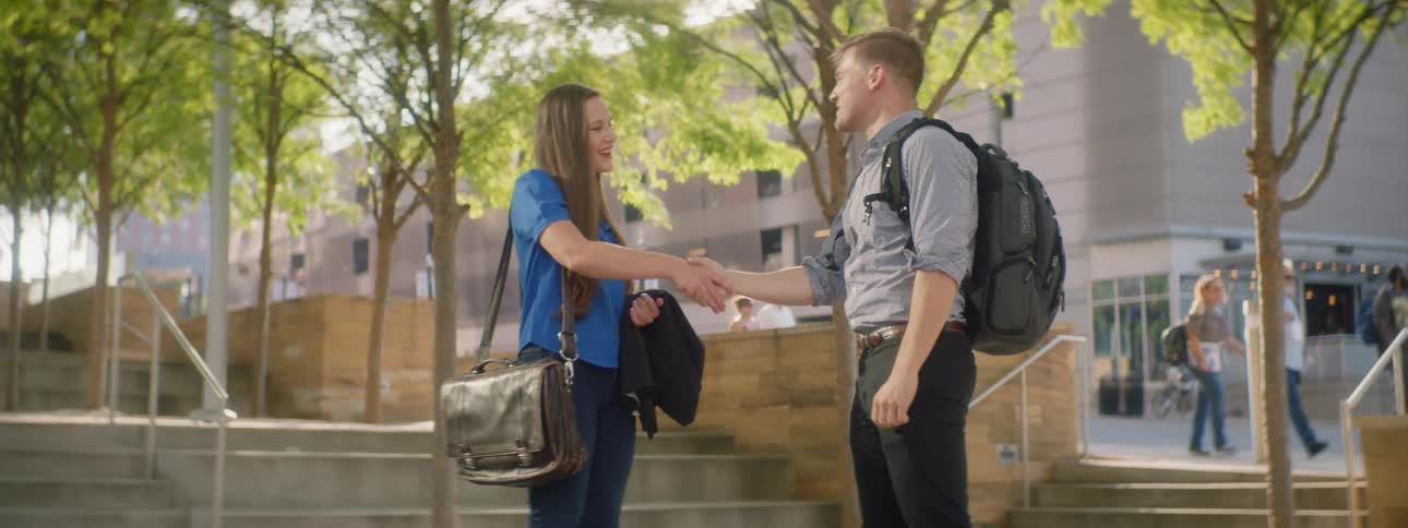 Man and woman talk and shake hands on college campus
