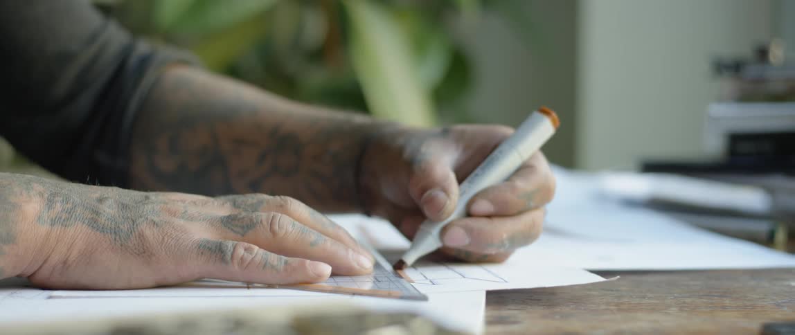 Person with tattoos on hands and arms draws a line with a marker