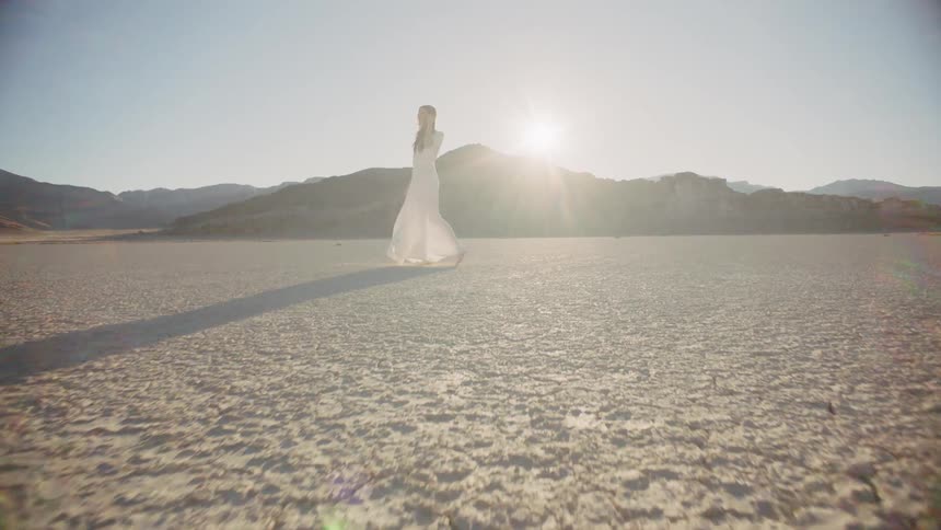 A woman standing outside in a long white dress near mountains