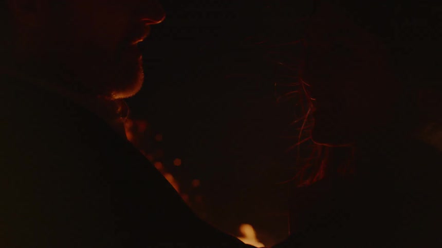 A man and woman hug while a fire burns around them