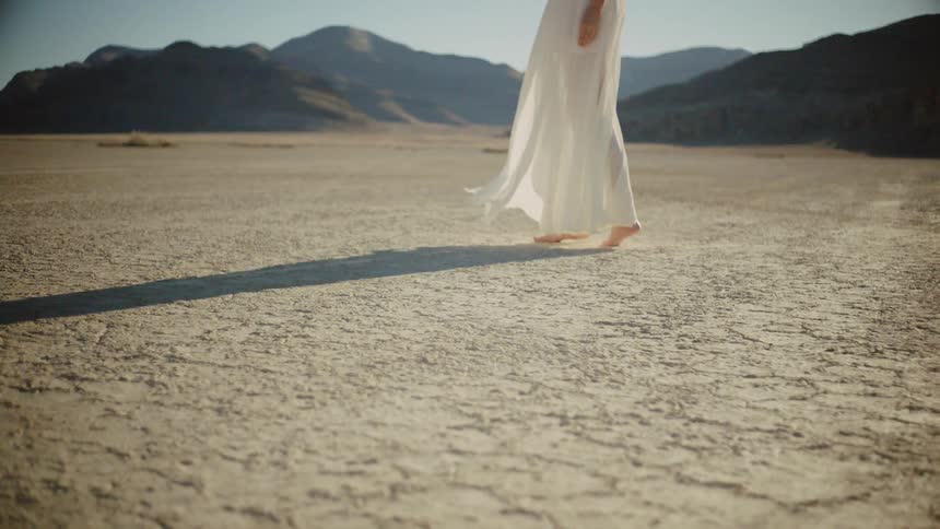 A woman standing outside in a long white dress as the wind blows her dress