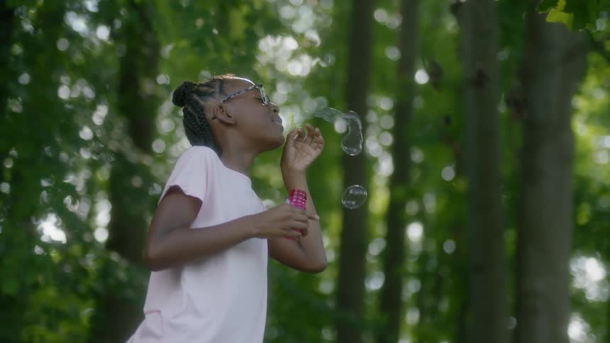 A pre teen girl blowing bubbles in a wooded area