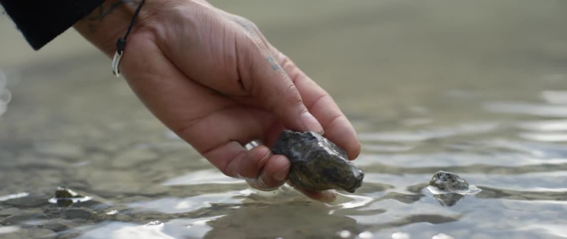 A hand is reaching into a river to pick up a small rock