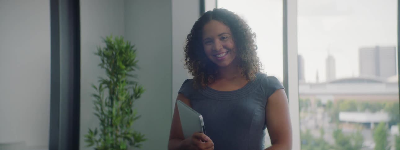 A woman smiling while holding a laptop in an office