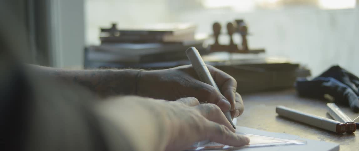 Man with tattoos on arm tracing something on a table with a marker