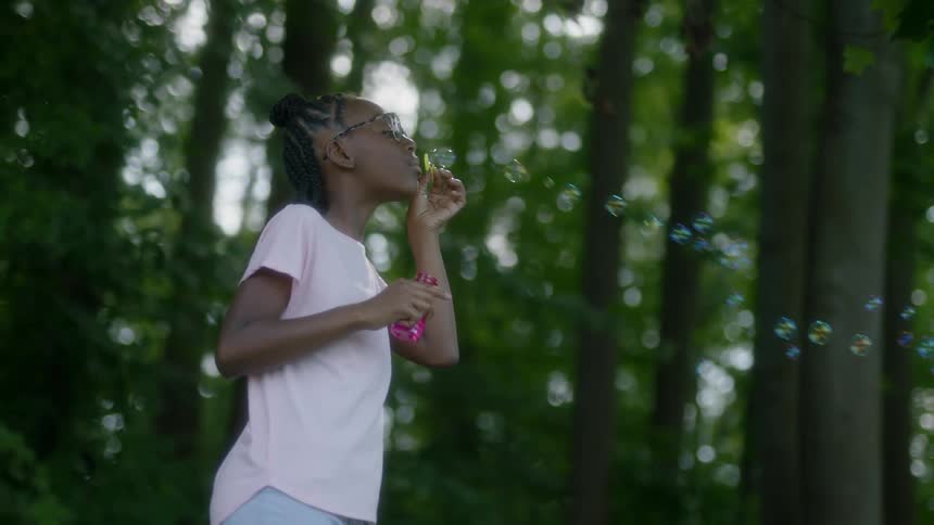 A young girl blows bubbles in the woods