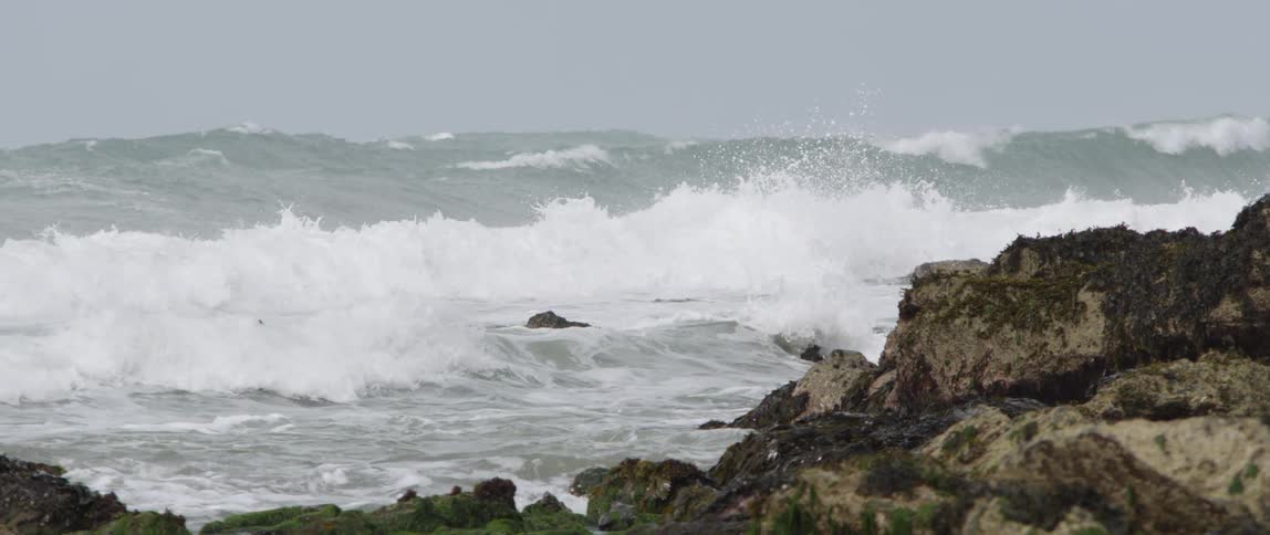 Water splashes onto large rocks on the beach