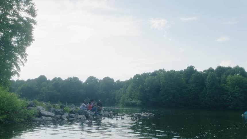 A family sitting next to a river feeding ducks