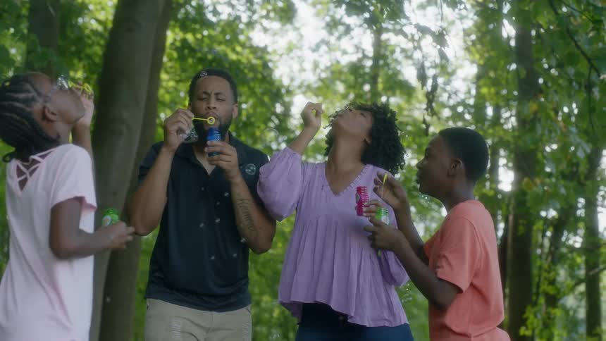 Family is blowing bubbles together in a park in the shade