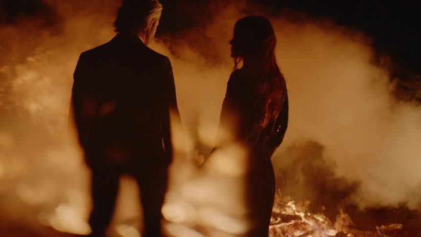 A man and woman hug in the midst of a burning fire