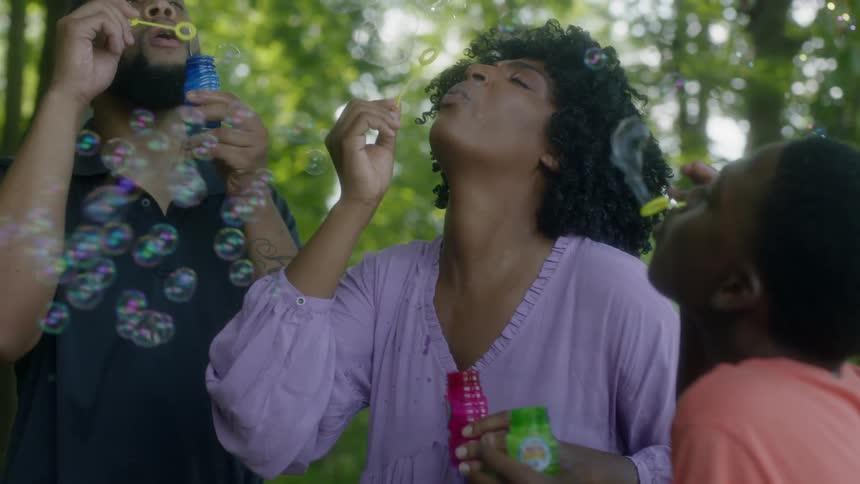 Parents and their kids all blow bubbles in the park
