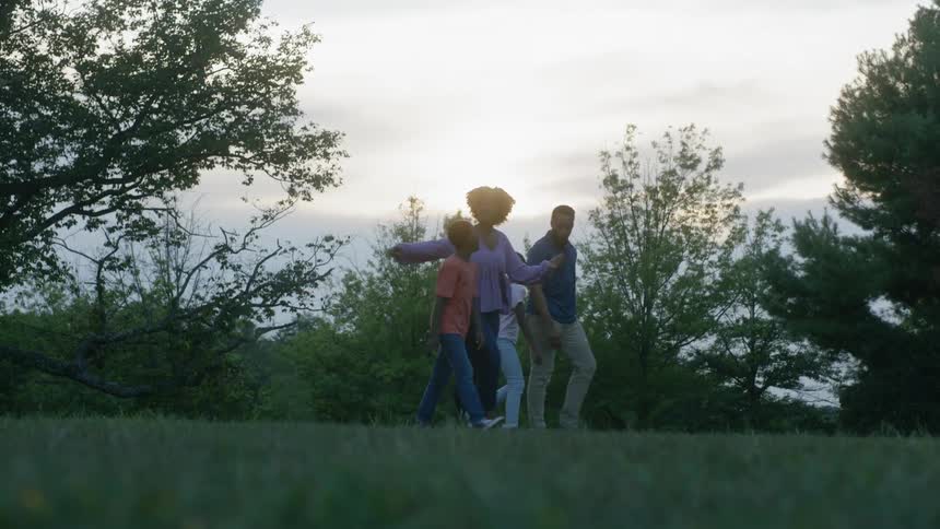 Family of four walks in a grassy field near trees
