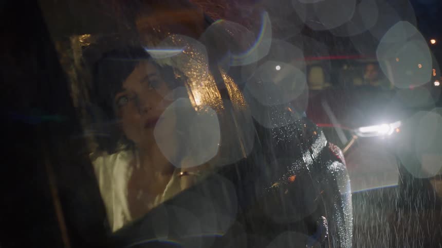 Woman sits in rear seat and glances out car window under downpour