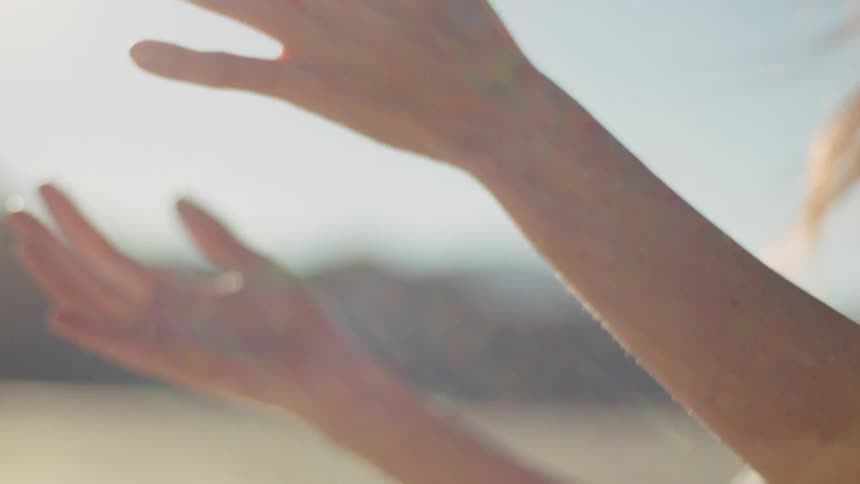 A woman with rings on her fingers raises her hands in the sunshine