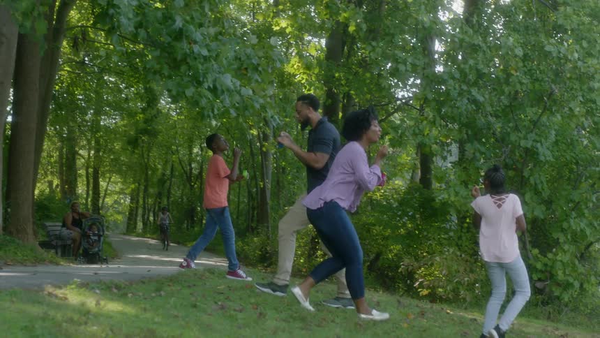 Family of four blows bubbles in a wooded area next to a river