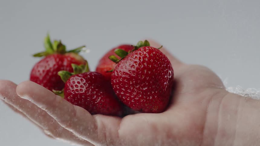 Mist falls around a hand holding red strawberries