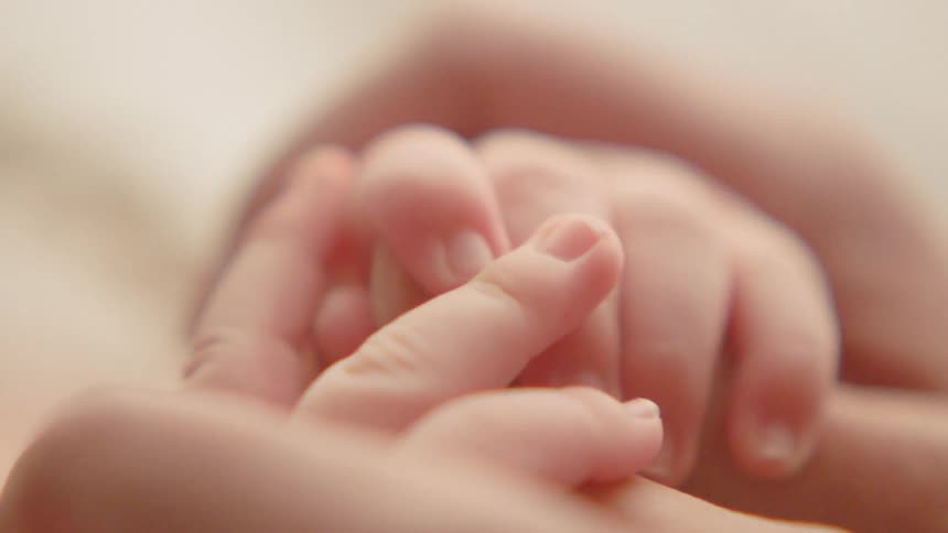 A woman holds a baby's hand