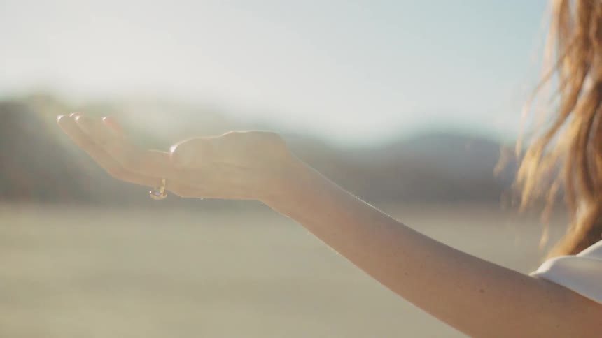 A woman standing in a sunny desert with her hand in the air
