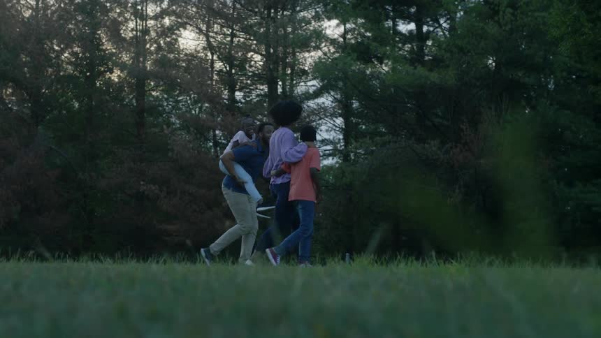 A mother daughter father and son walking through a park with the little girl riding piggyback on dad