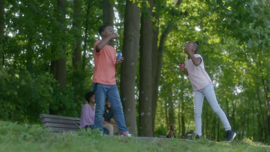 Two young kids blow bubbles outside in nature