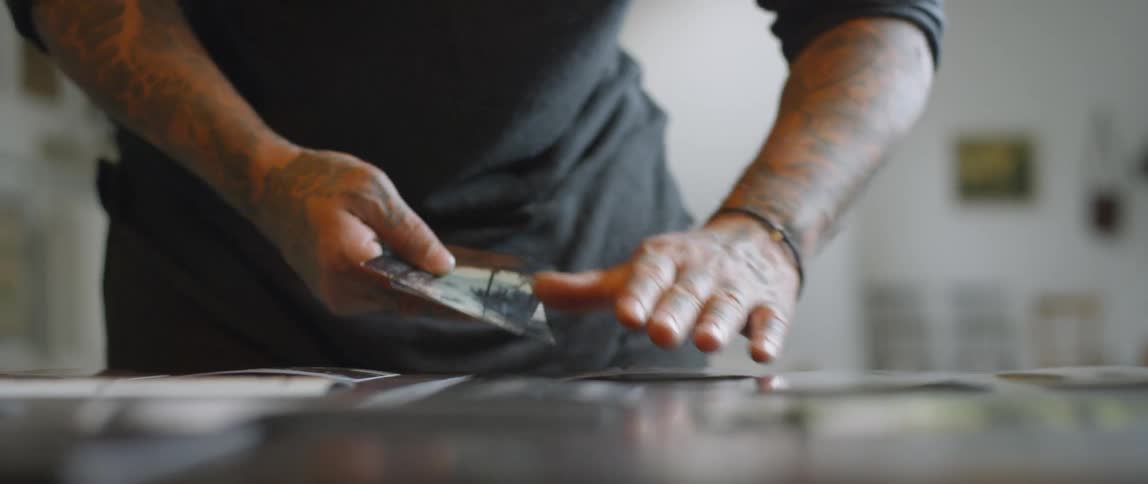 Man with many tattoos picking up photographs from a table