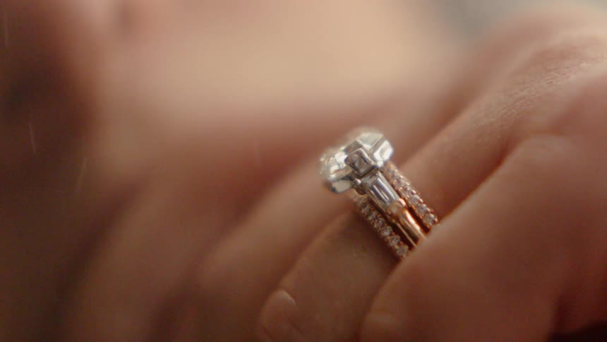A person's hand that has a diamond ring on it that is front of falling snow