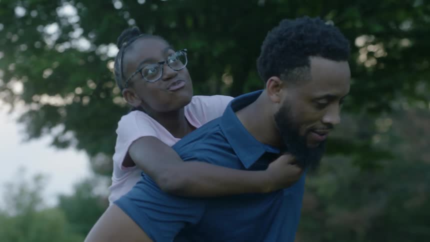 A young girl rides on her fathers back as they walk