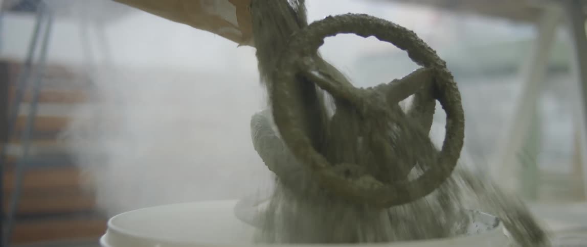 Dust swirls while concrete mix is poured into a plastic bucket
