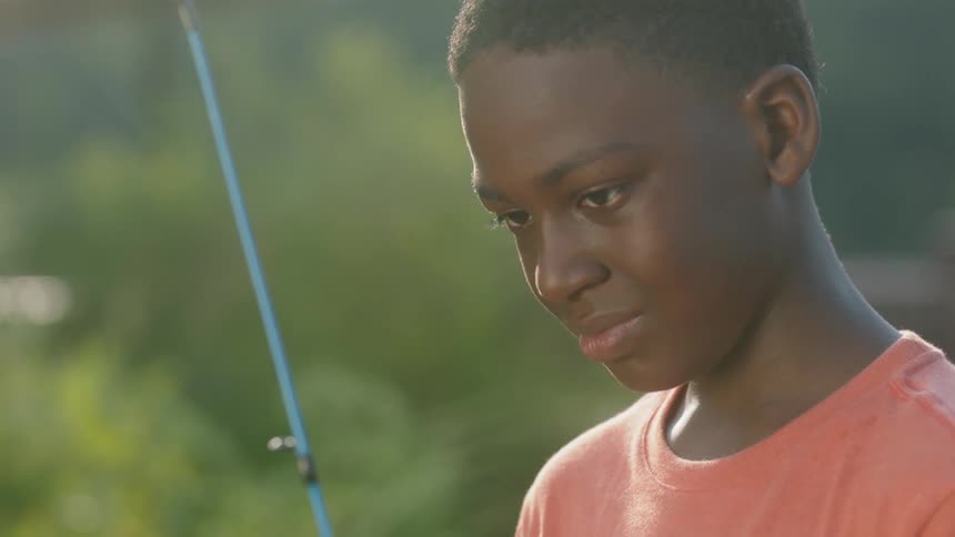 A young boy holds a fishing rod outside