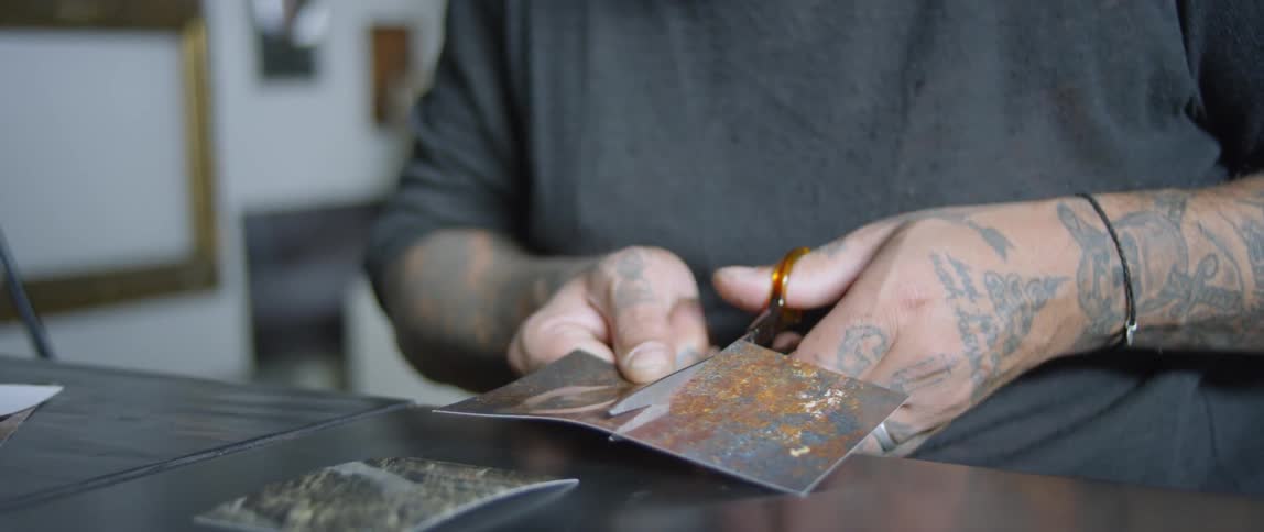 Tattooed hands cut a piece of paper with scissors