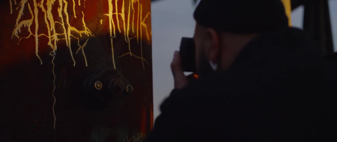 A man takes a close up photograph of a column with graffiti on it
