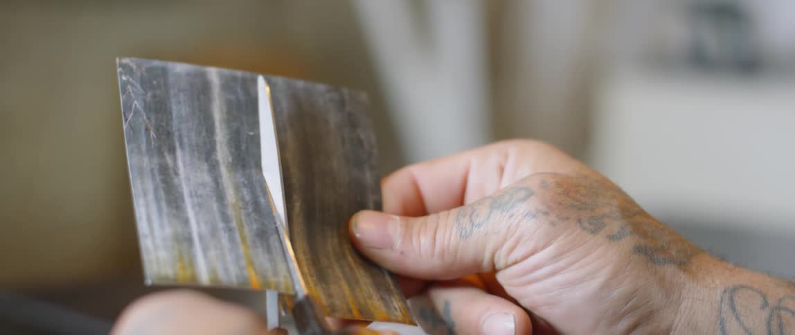 Tattooed hands cut a piece of paper with scissors