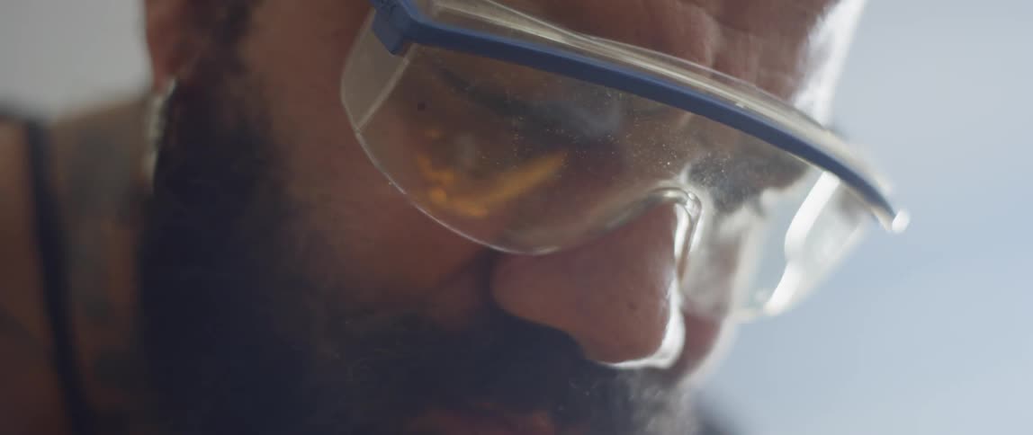A bearded man welds wearing protective goggles