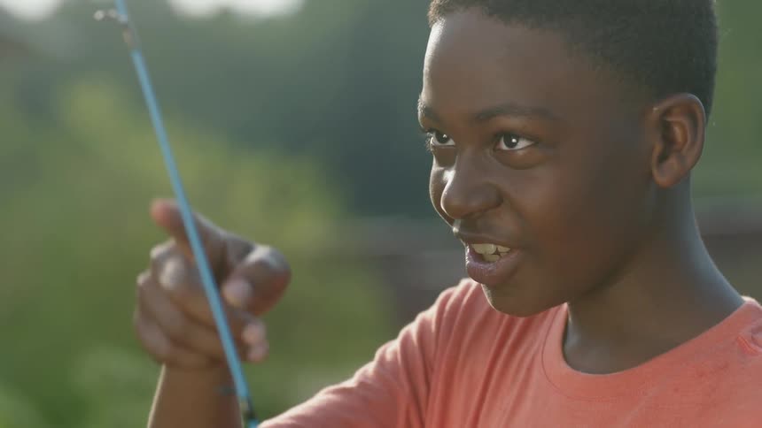 Boy is talking and smiling while holding fishing pole outdoors