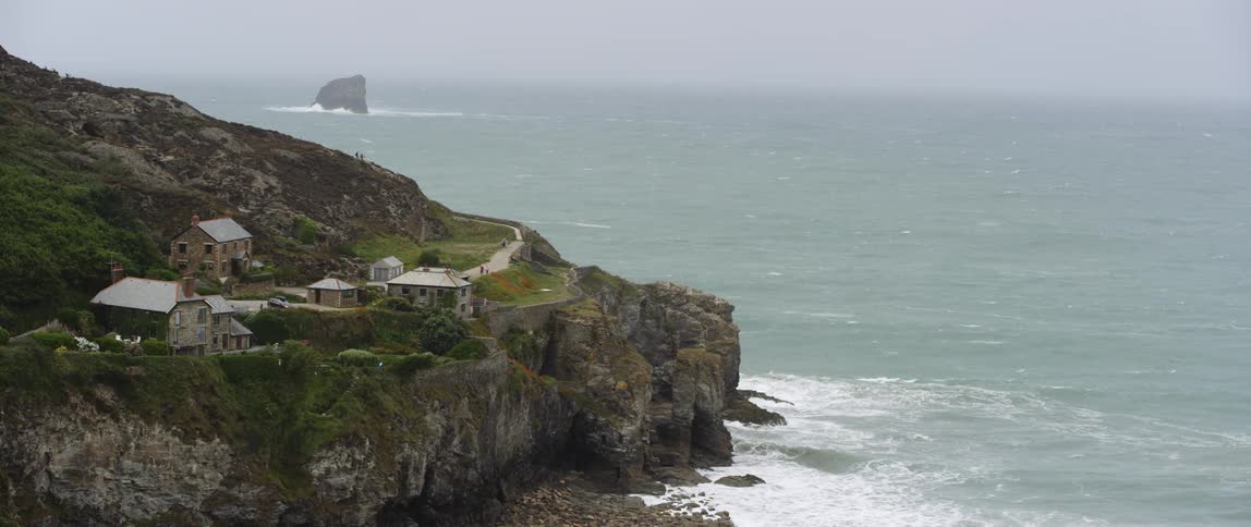 Several houses on a cliffside near crashing waves and rocks