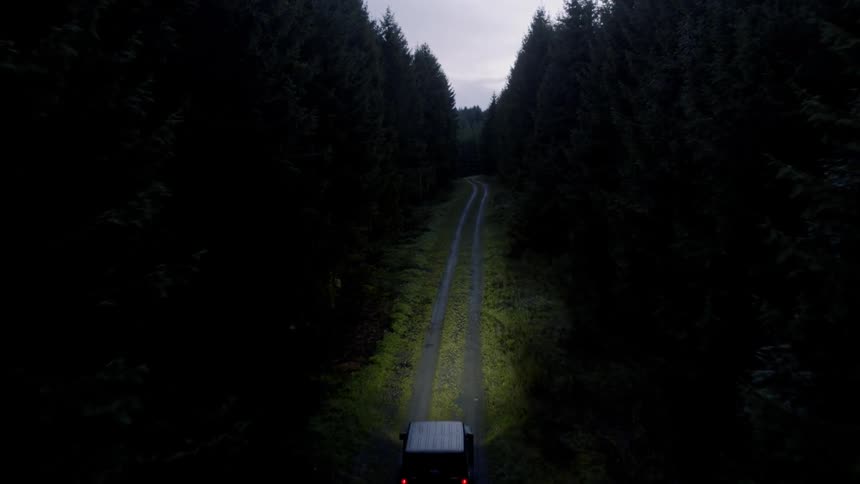 A jeep driving down a forest road in the dark