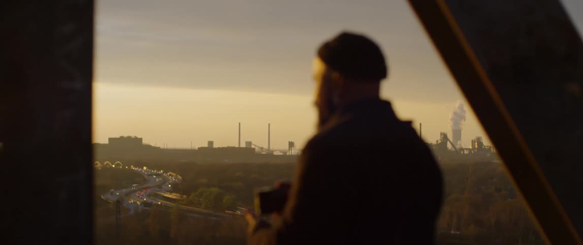 A man looking at the town and then down to his camera