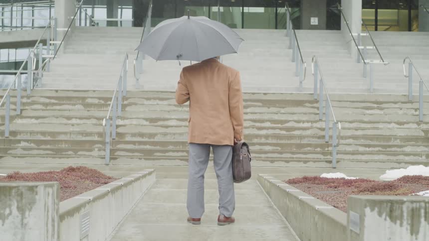 A man holding an umbrella and satchel looks towards a staircase