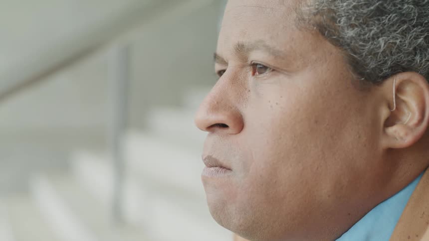A man sits on stairs and looks around before looking down in sadness