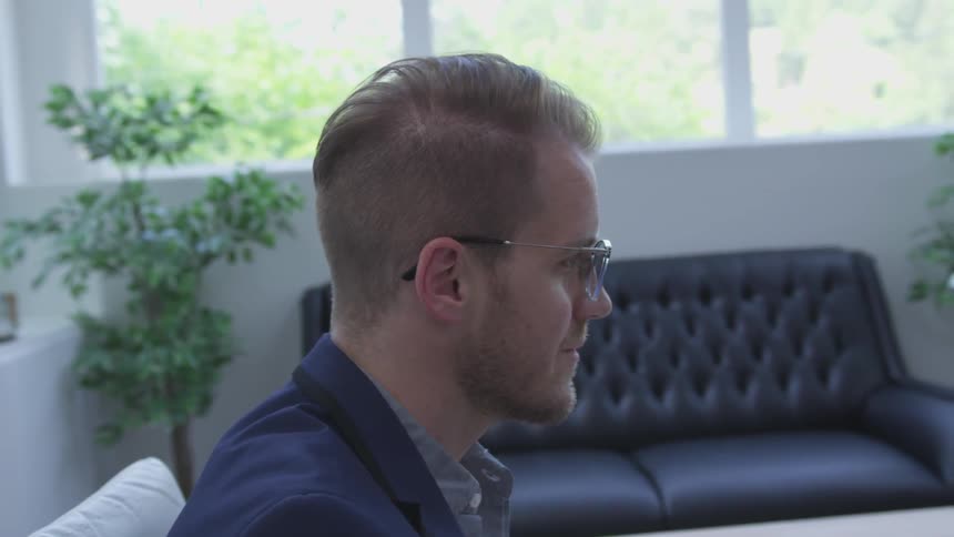 A man wearing glasses smiles at something in front of him