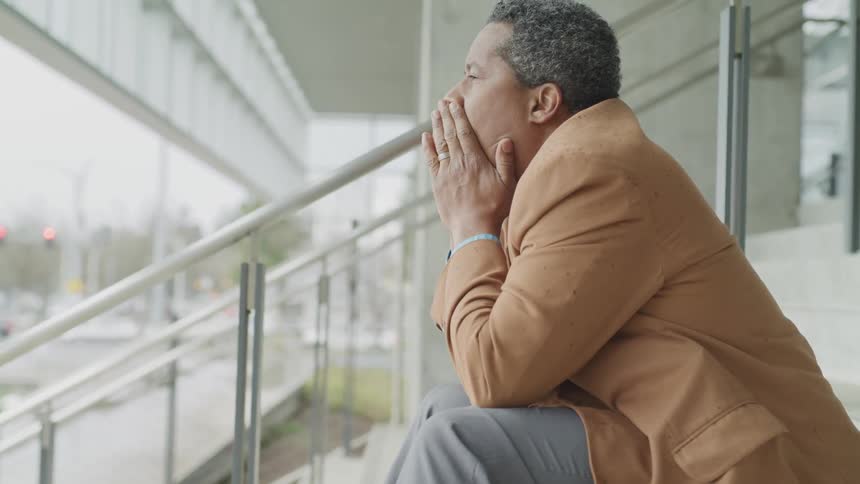 Man in suit sits and rubs face with hands while staring into the distance